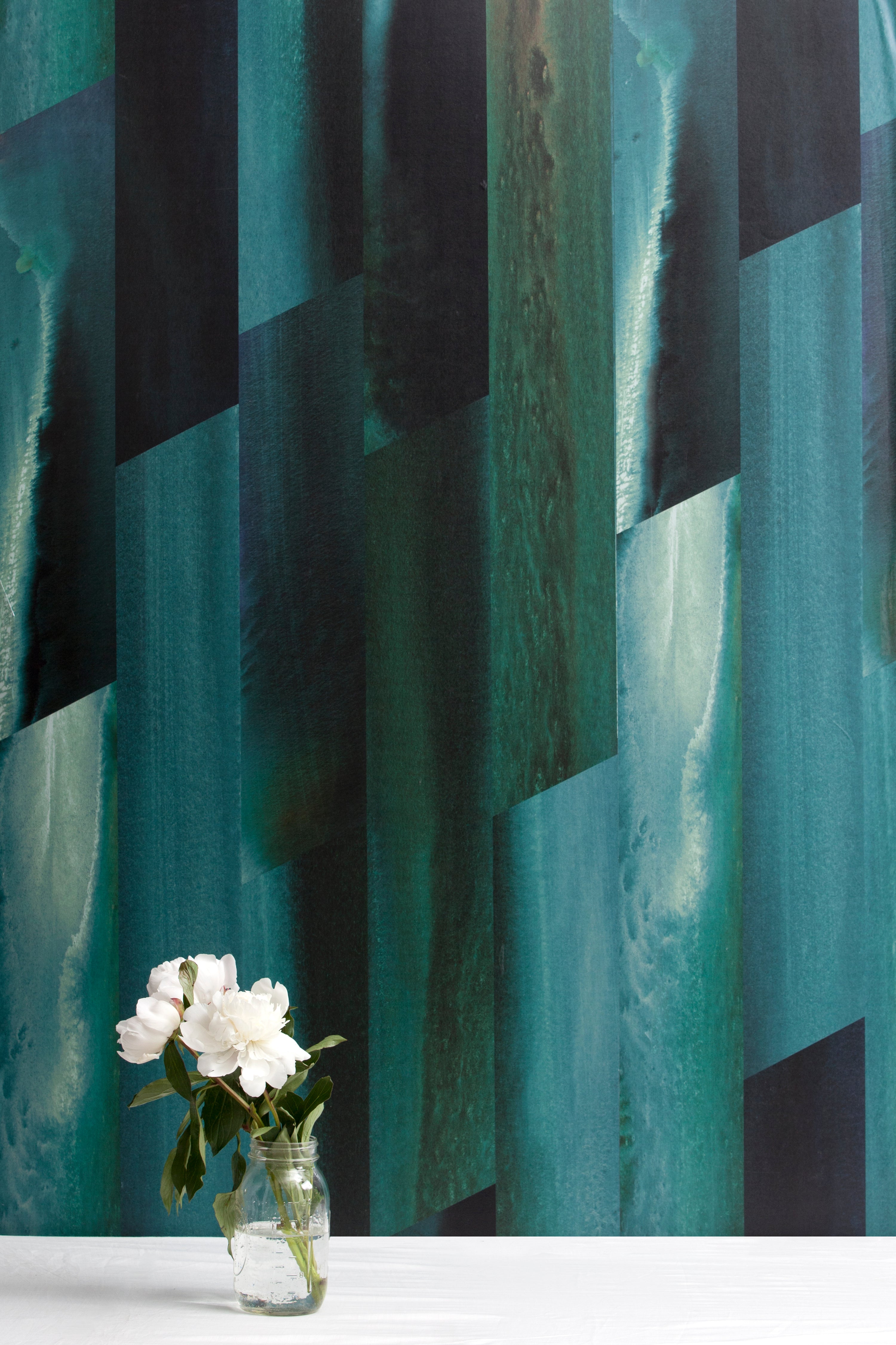 A vase of flowers stands in front of a wall papered in a linear geometric print in shades of black, blue and turquoise.