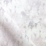 Detail of fabric in a painterly tree print in light pink and purple on a cream field.