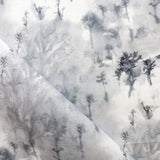 Detail of fabric in a painterly tree print in gray and charcoal on a white field.