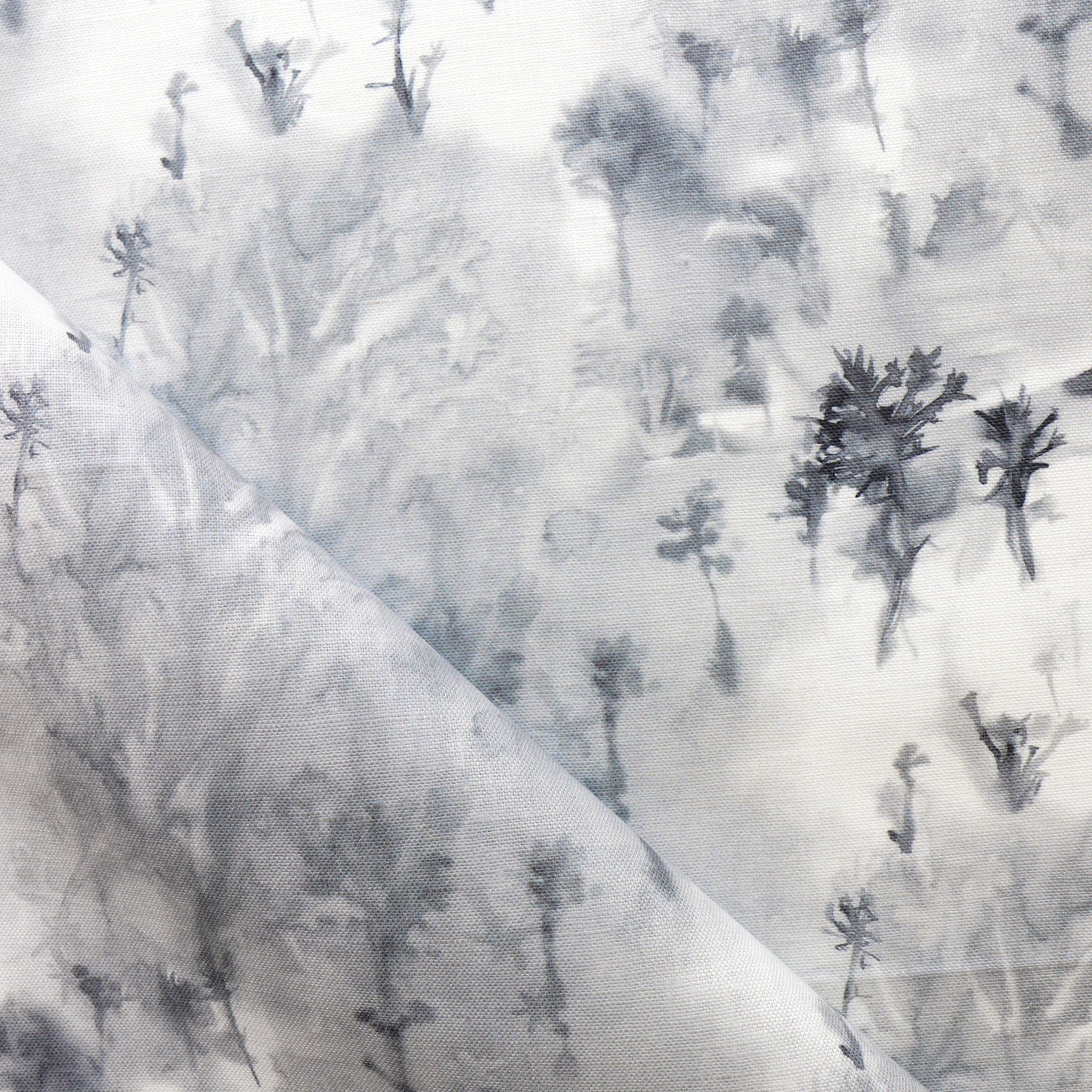 Detail of fabric in a painterly tree print in gray and charcoal on a white field.