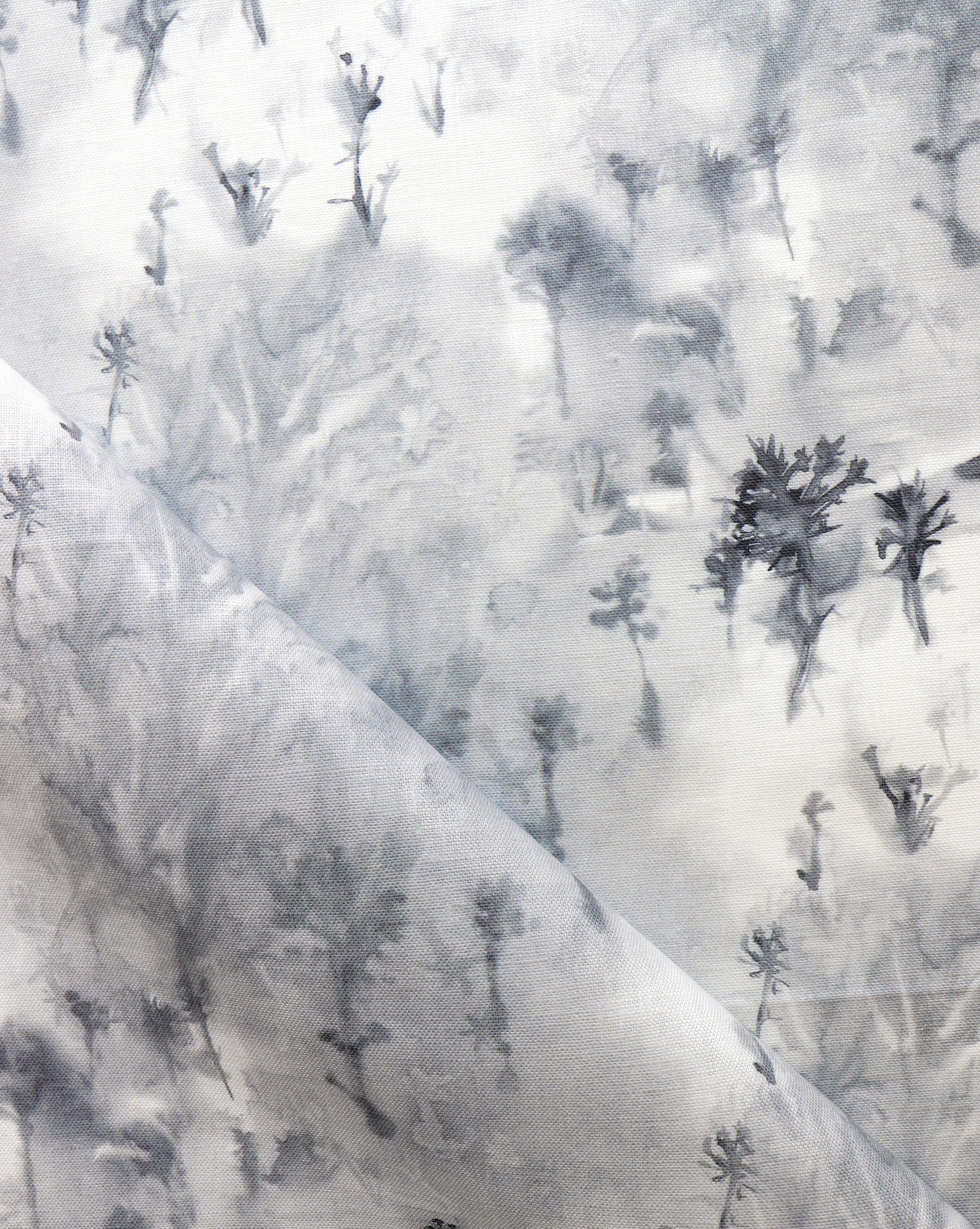 Detail of fabric in a painterly tree print in gray and charcoal on a white field.