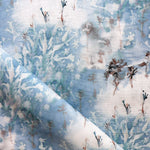 Detail of fabric in a painterly tree print in blue, gray and tan on a white field.