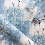 Detail of fabric in a painterly tree print in blue, gray and tan on a white field.