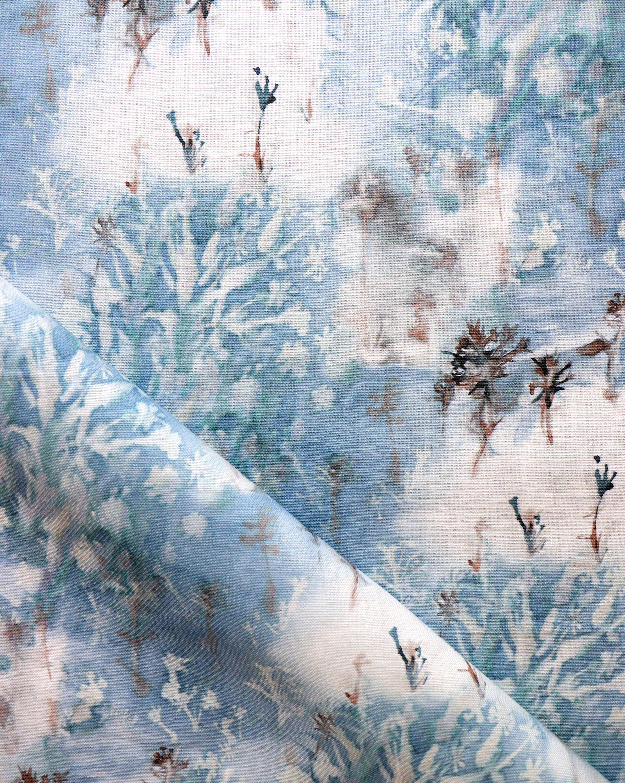 Detail of fabric in a painterly tree print in blue, gray and tan on a white field.