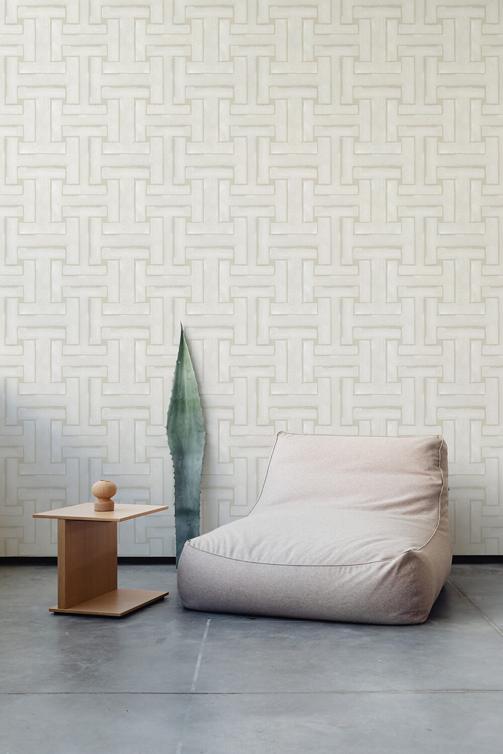 A plush chair and end table stand in front of a wall papered in a large-scale geometric print in cream.