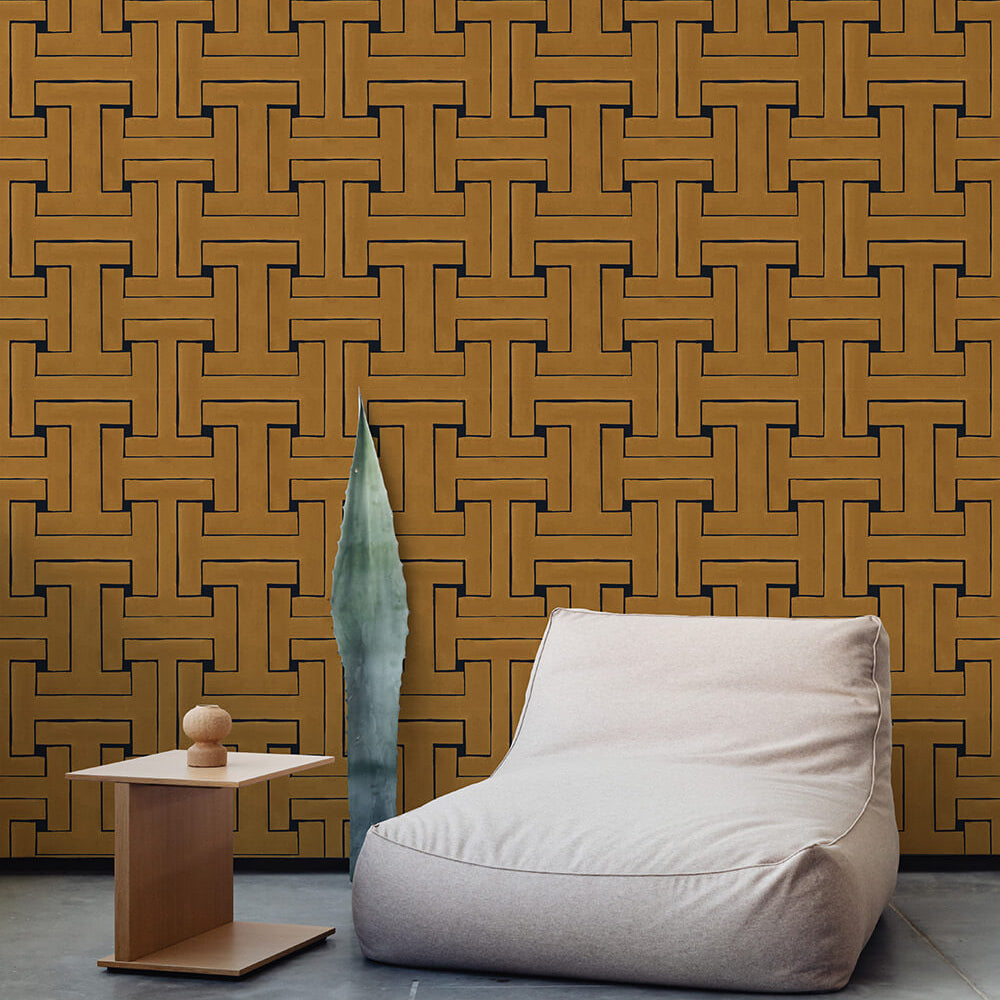 A plush chair and end table stand in front of a wall papered in a large-scale geometric print in gold and black.