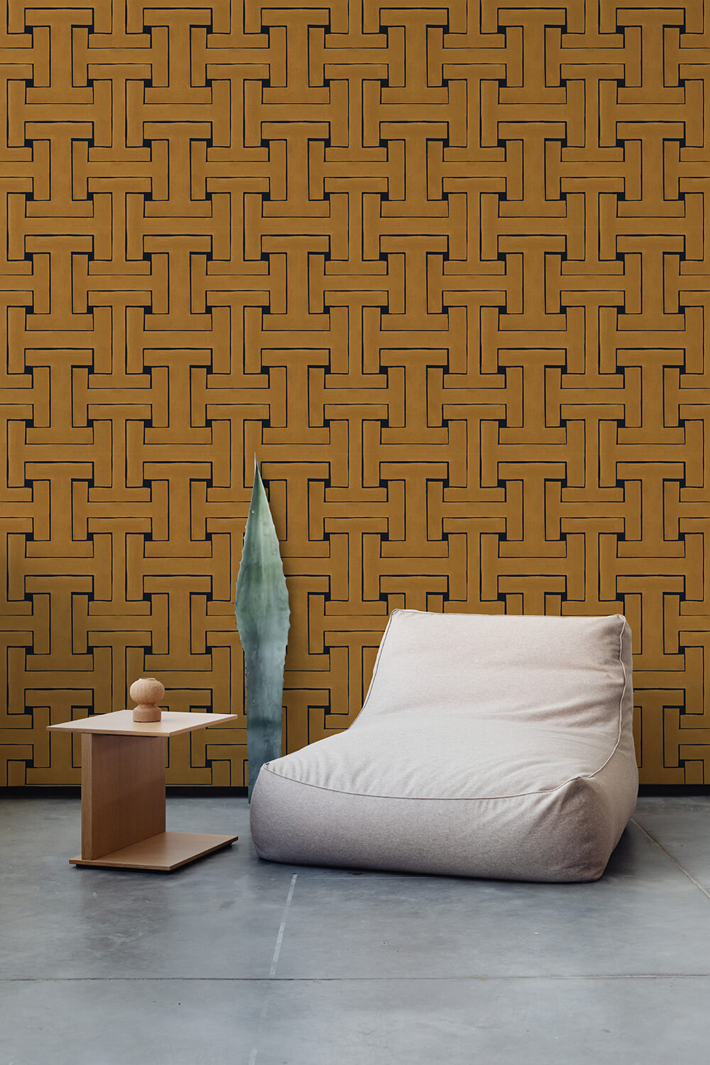 A plush chair and end table stand in front of a wall papered in a large-scale geometric print in gold and black.