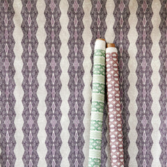 A wall papered in a geometric black and purple pattern on a cream background. Two other rolls of wallpaper lean against it.