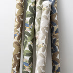 A group of fabric rolls leaned against a wall, all in different colorways of the same botanical and parrot print.