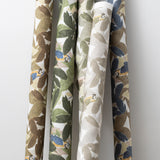 A group of fabric rolls leaned against a wall, all in different colorways of the same botanical and parrot print.