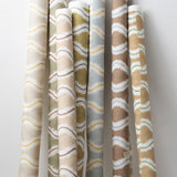 A group of fabric rolls leaned against a wall, all in different colorways of the same curvy stripe print.