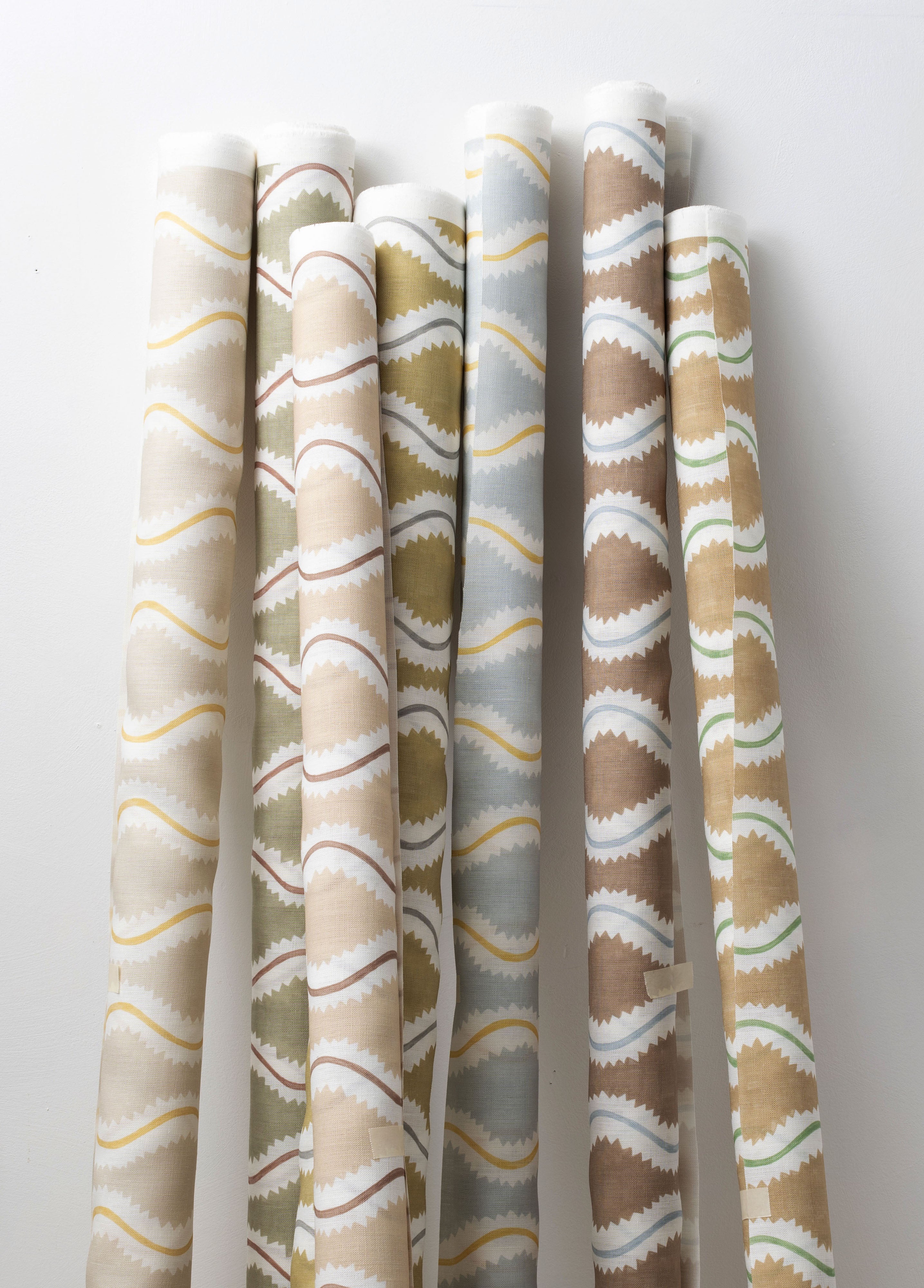 A group of fabric rolls leaned against a wall, all in different colorways of the same curvy stripe print.