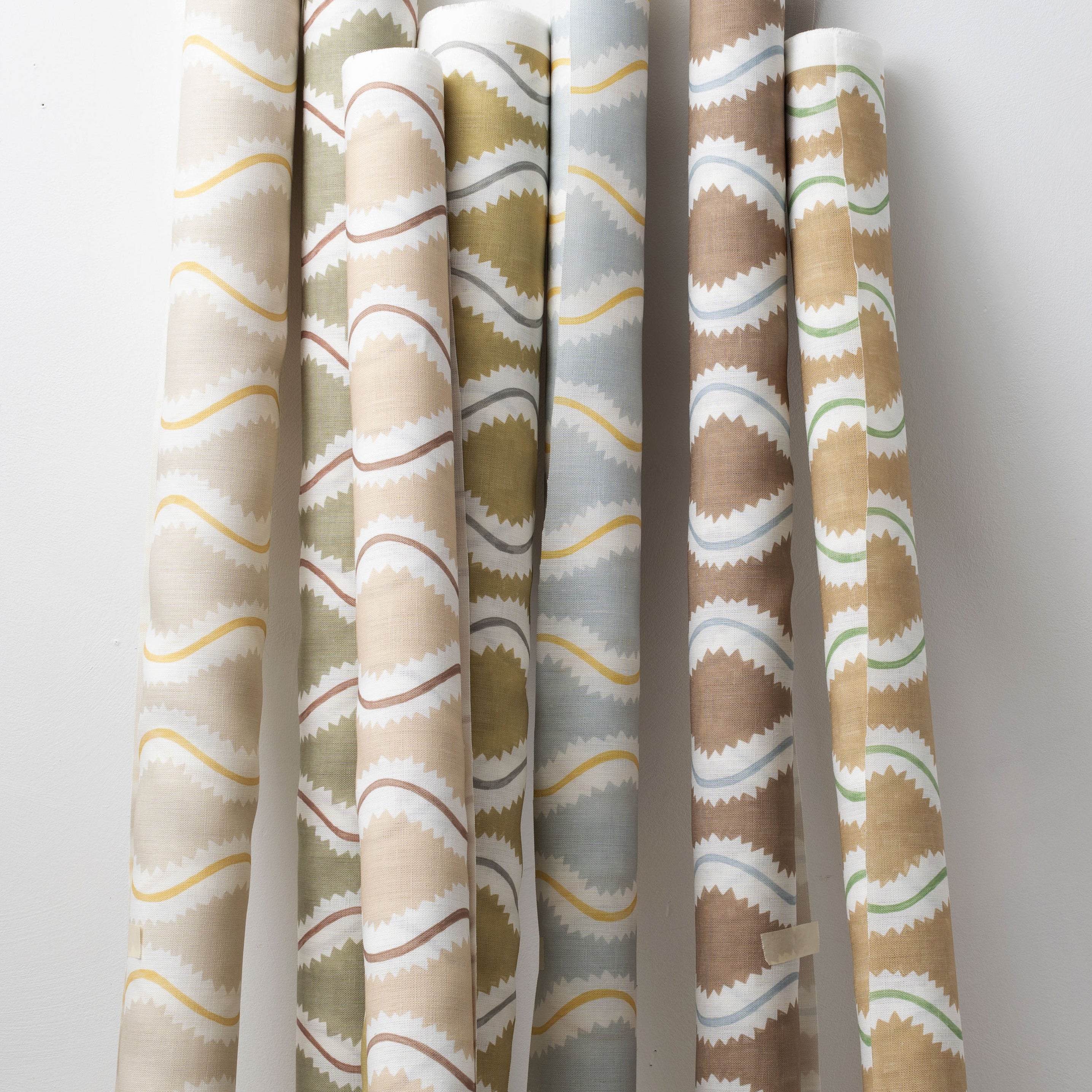 A group of fabric rolls leaned against a wall, all in different colorways of the same curvy stripe print.