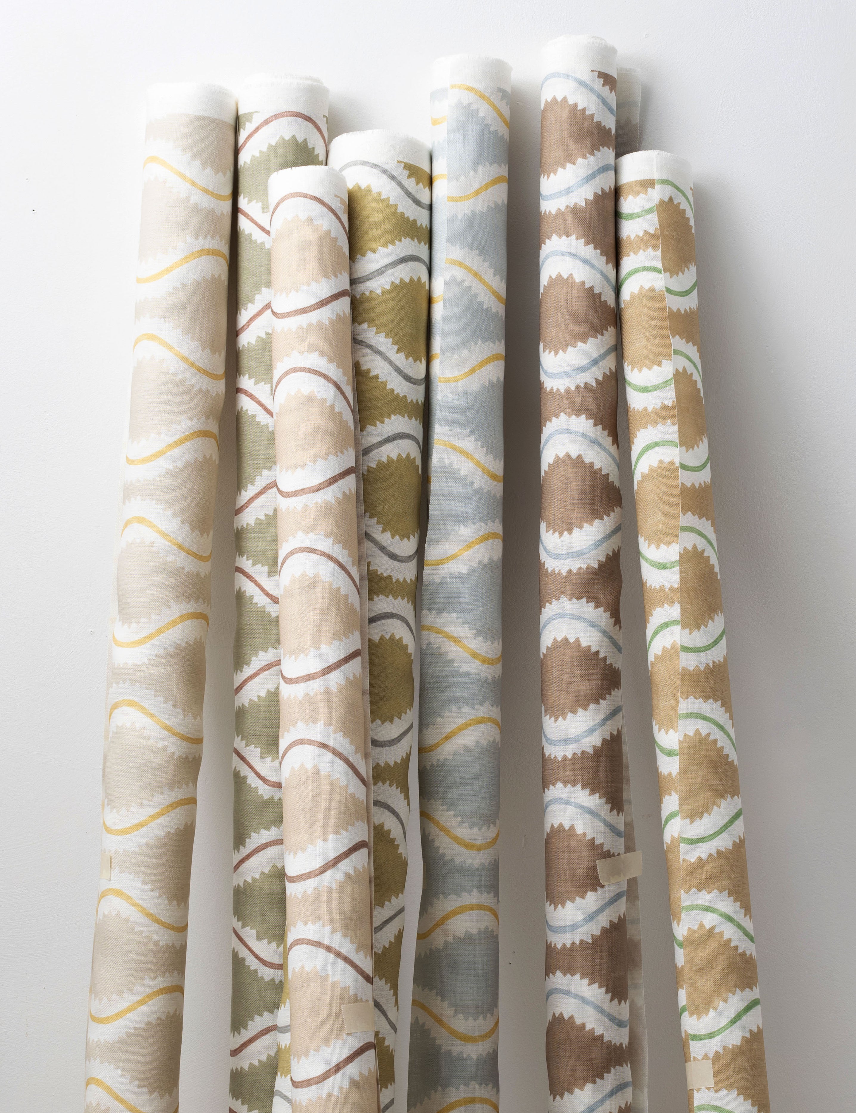 A group of fabric rolls leaned against a wall, all in different colorways of the same curvy stripe print.