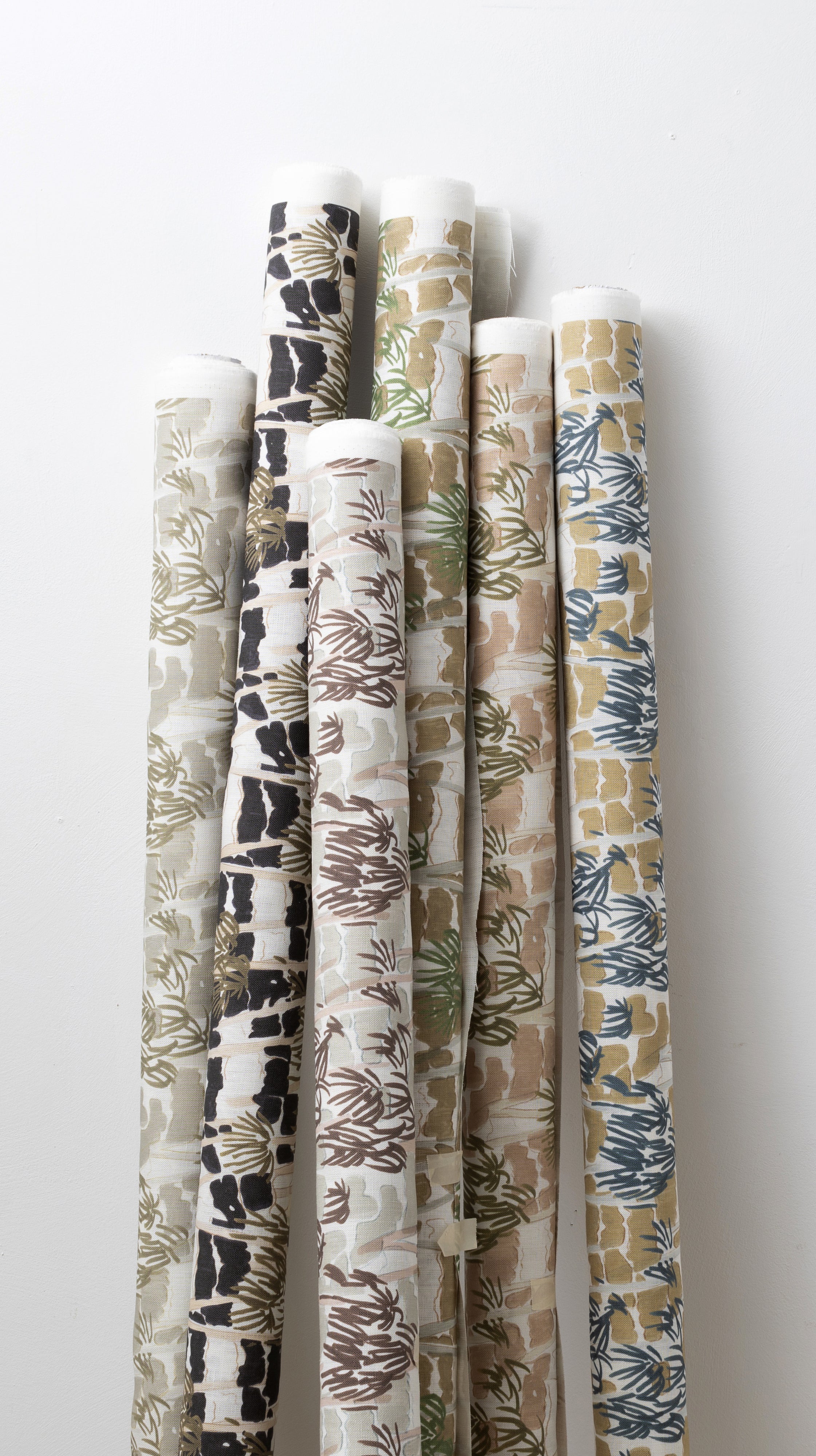 A group of fabric rolls leaned against a wall, all in different colorways of the same painterly palm tree print.