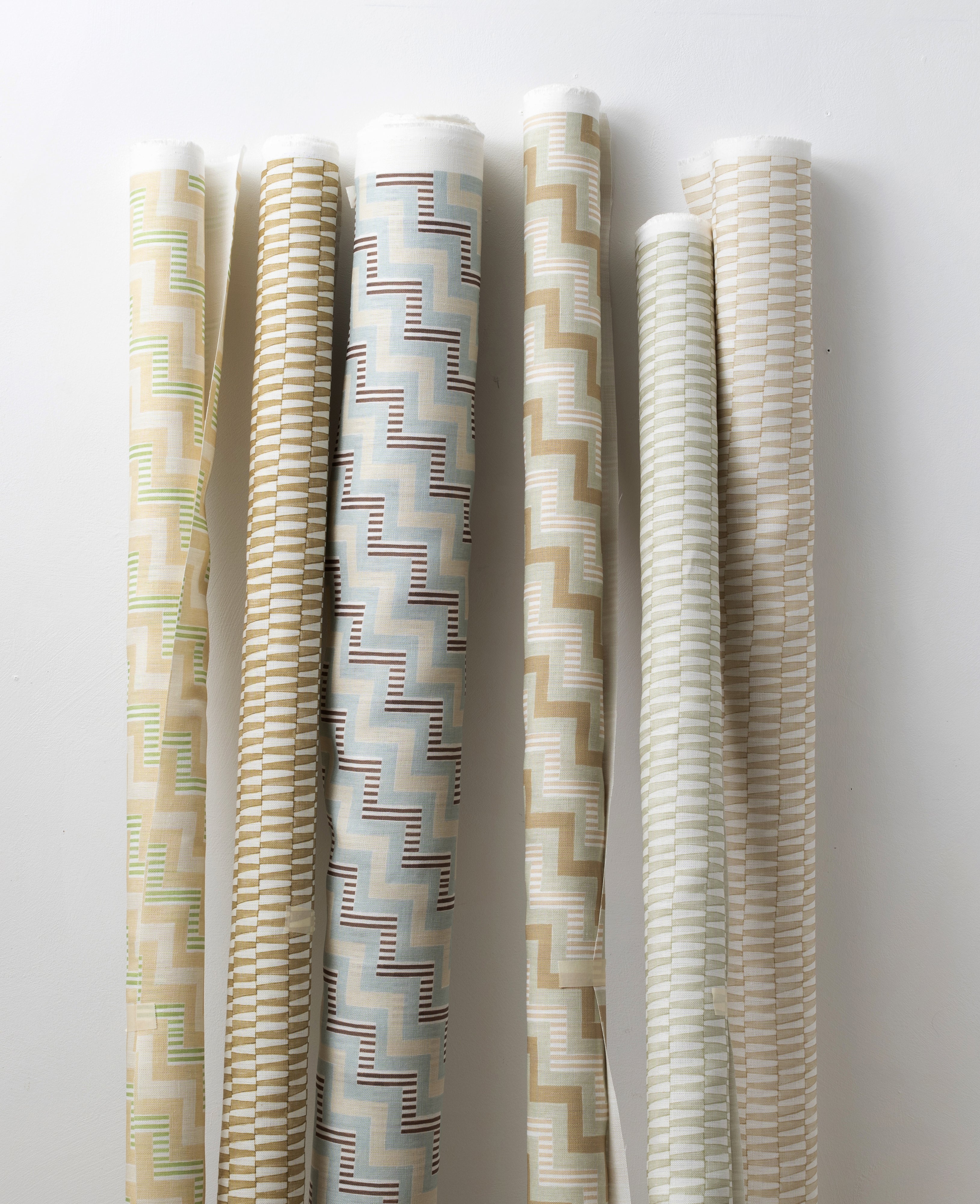 A group of fabric rolls leaned against a wall, all in different colorways of the same geometric stripe print.