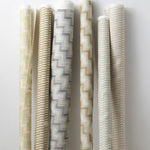 A group of fabric rolls leaned against a wall, all in different colorways of the same triangular stripe print.