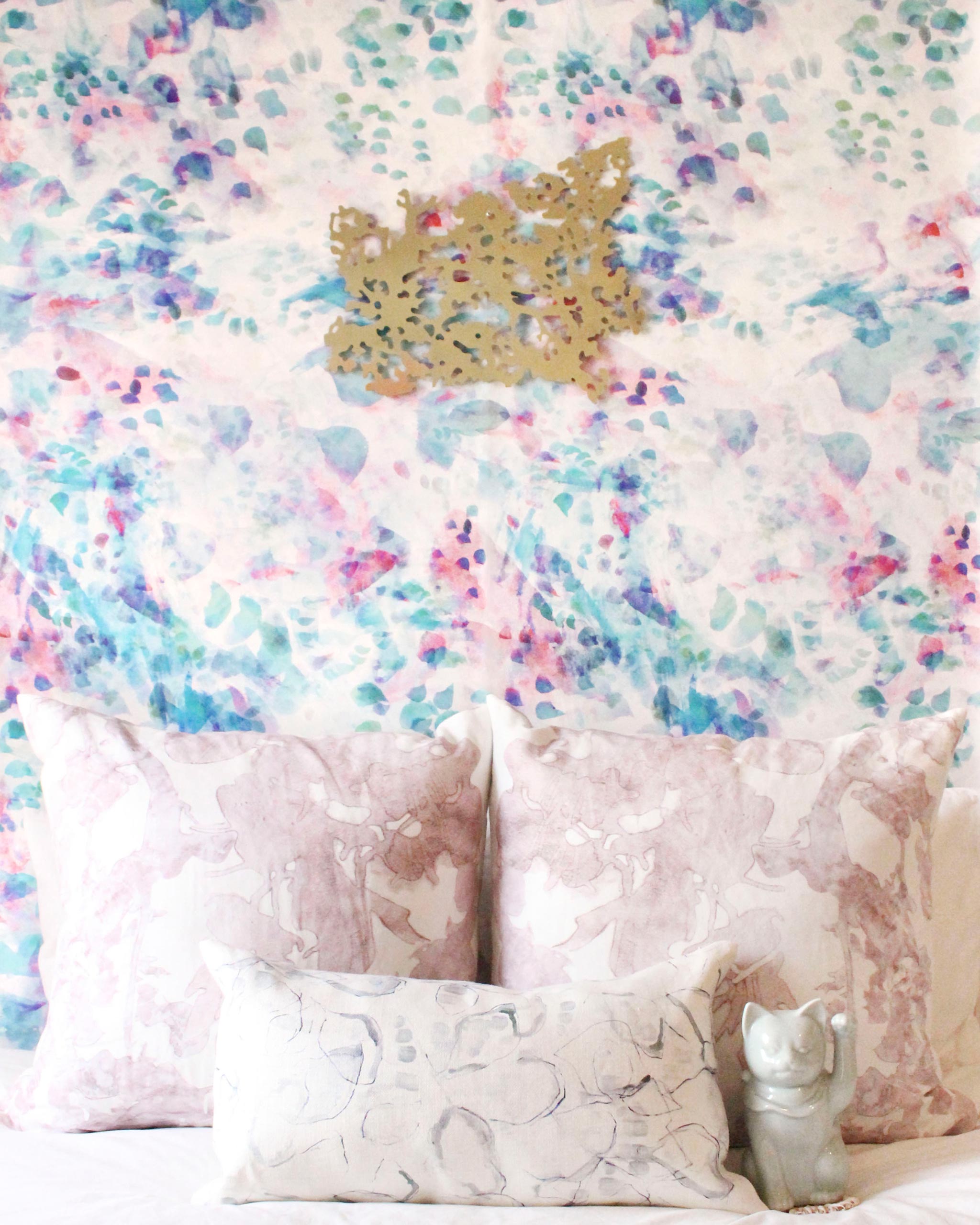 A pink couch stands in front of a wall papered in an abstract paint blotch print in pink, green, turquoise and white.