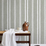 A bench with a towel and clay vases stands in front of a wall papered in a textural stripe pattern in white and greige.