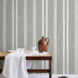 A bench with a towel and clay vases stands in front of a wall papered in a textural stripe pattern in white and greige.