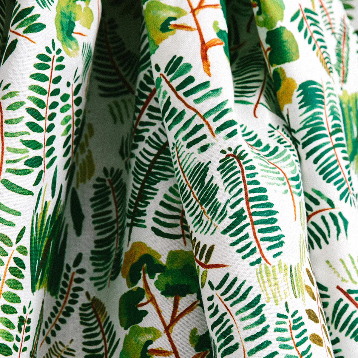 Draped fabric yardage in a painterly botanical print in shades of green and yellow on a white field.