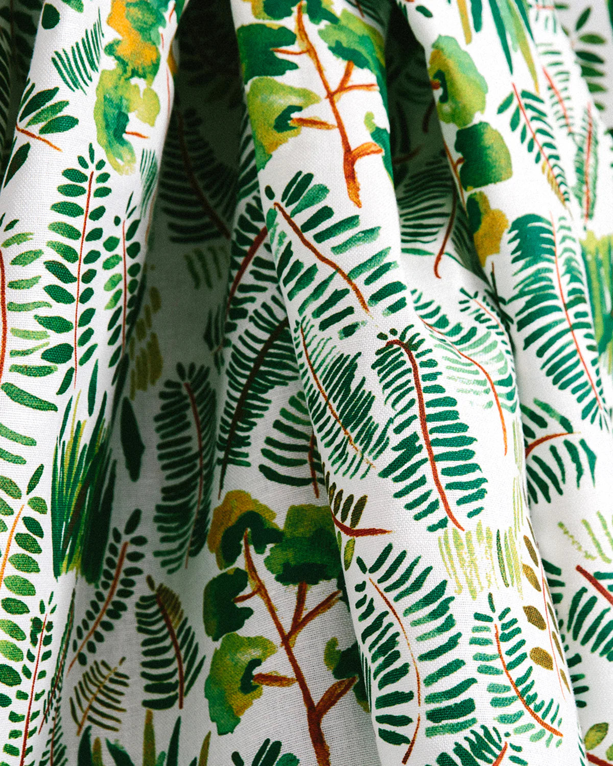 Draped fabric yardage in a painterly botanical print in shades of green and yellow on a white field.