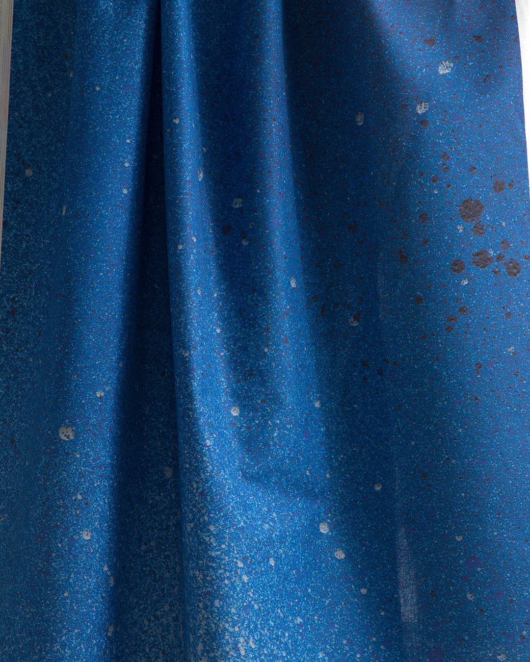 Draped fabric yardage in an abstract ombré paint splatter print in shades of blue and gray.