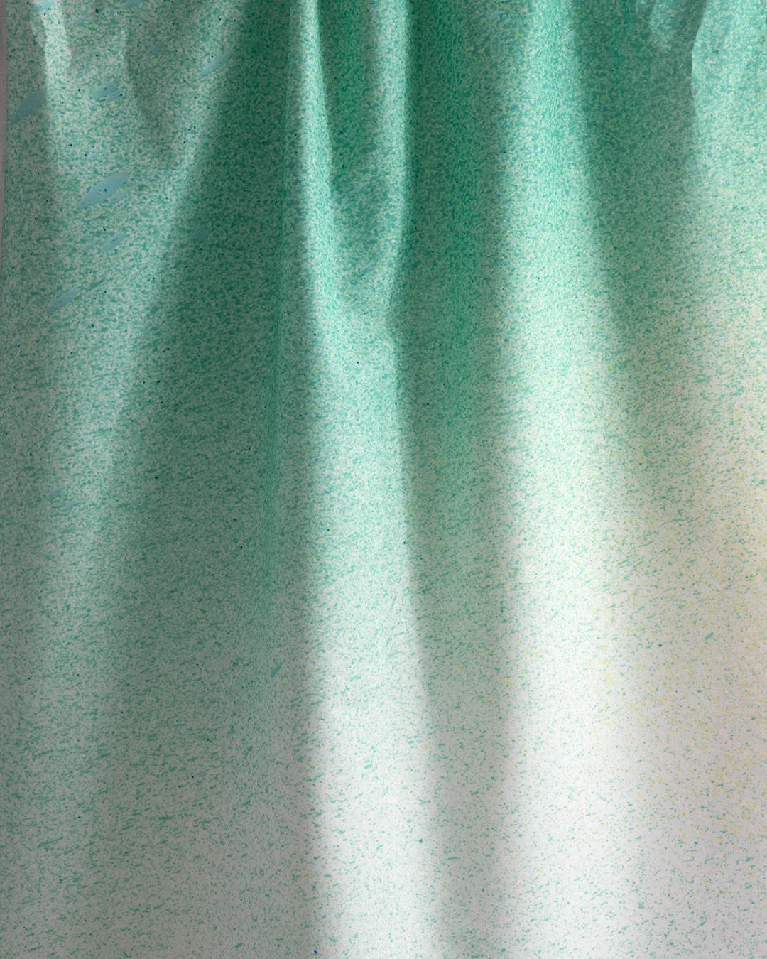 Draped fabric yardage in an abstract ombré paint splatter print in shades of turquoise, green and white.