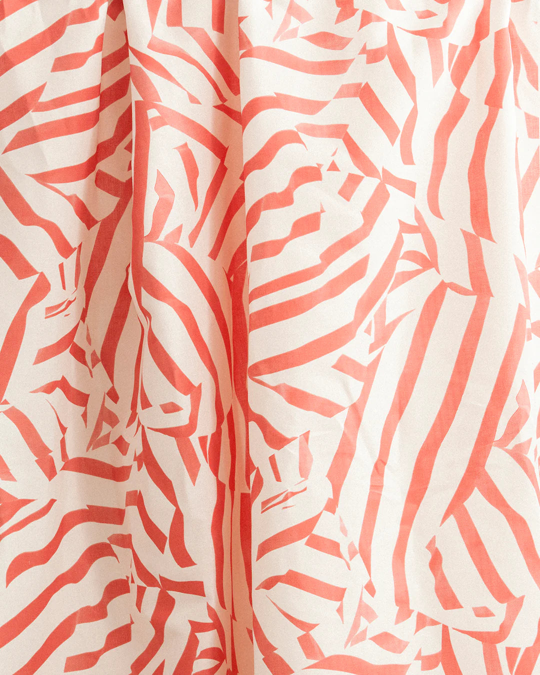 Draped fabric yardage in a playful broken stripe print in coral on a cream field.