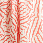 Draped fabric yardage in a playful broken stripe print in coral on a cream field.