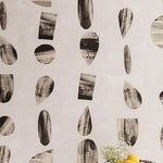 A bowl of fruit stands in front of a wall papered in an abstract curvolinear pattern in black, white and gray.