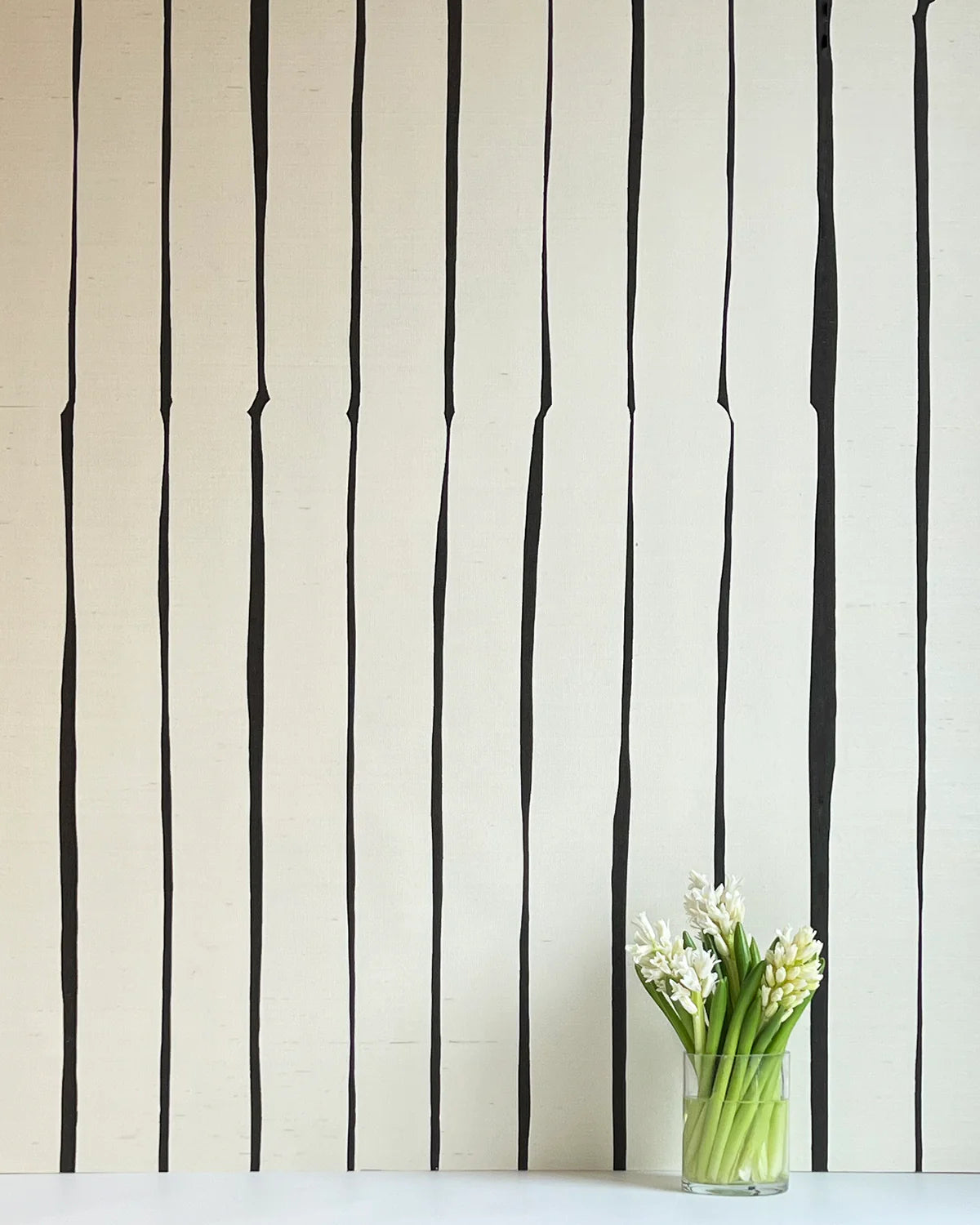 A vase of flowers stands in front of a wall covered in a playful irregular stripe print in black on a cream field.