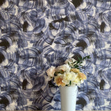 A vase of flowers stands in front of a wall papered in an abstract paint swatch print in black and navy on a cream field.