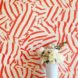 A vase of flowers stands in front of a wall papered in a playful broken stripe print in red on a cream field.