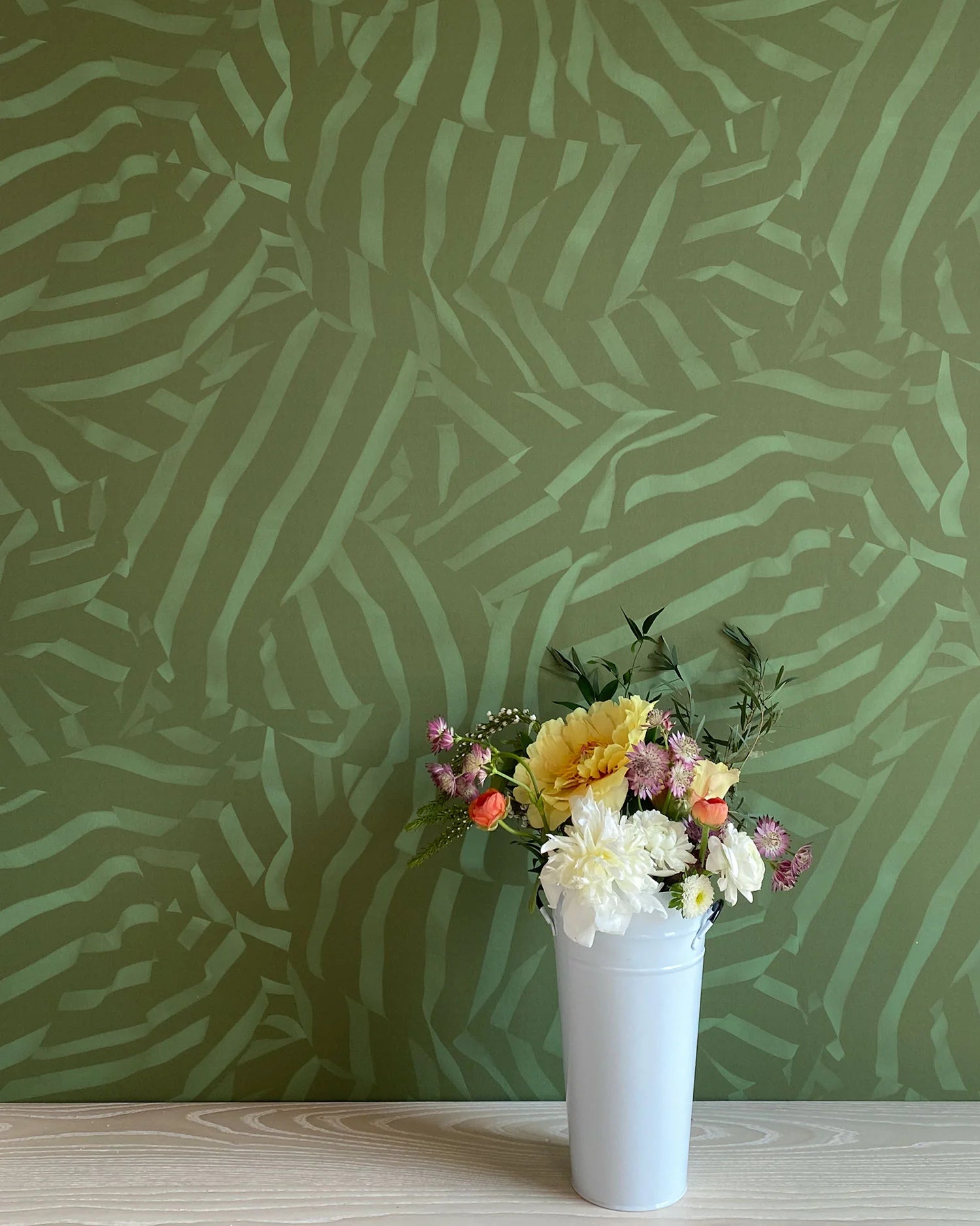 A vase of flowers stands in front of a wall papered in a playful broken stripe print in dark green on a green field.