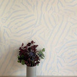 A vase of flowers stands in front of a wall papered in a playful broken stripe print in light blue on a cream field.