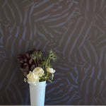 A vase of flowers stands in front of a wall papered in a playful broken stripe print in black on a navy field.