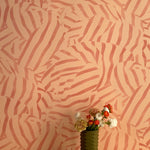 A vase of flowers stands in front of a wall papered in a playful broken stripe print in rust on an orange field.