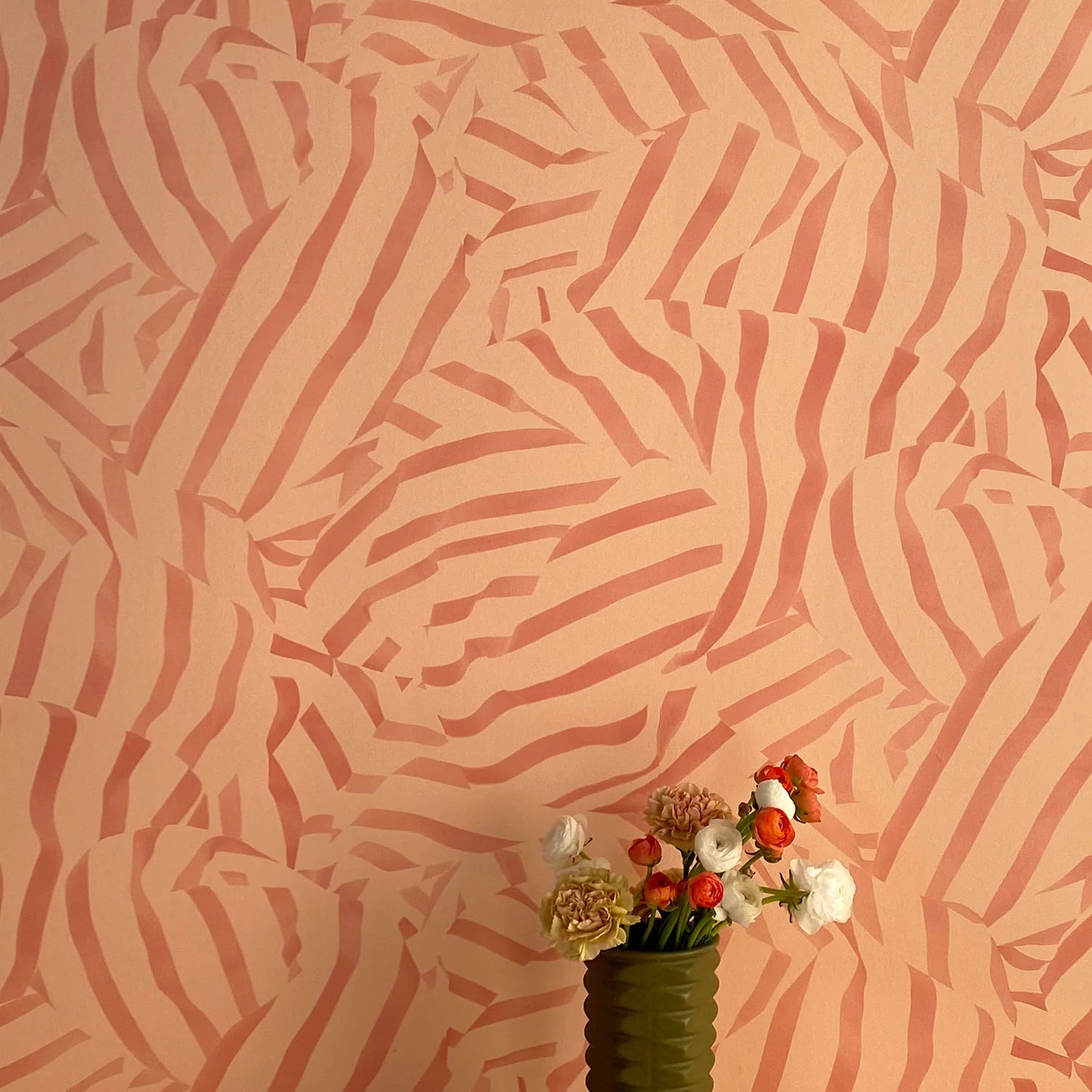 A vase of flowers stands in front of a wall papered in a playful broken stripe print in rust on an orange field.