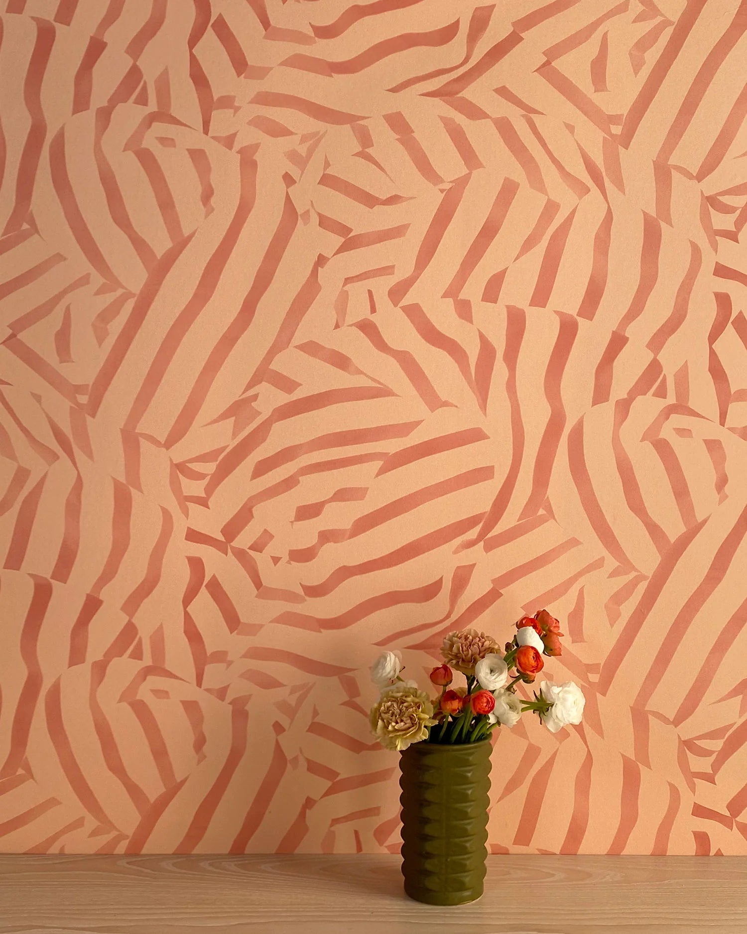 A vase of flowers stands in front of a wall papered in a playful broken stripe print in rust on an orange field.