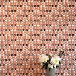 A vase of flowers stands in front of a wall papered in a linear floral print in red, white and black on an orange field.