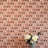 A vase of flowers stands in front of a wall papered in a linear floral print in red, white and black on an orange field.