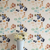 A vase of flowers stands in front of a wall papered in an abstract painterly print in turquoise, blue, orange and white.