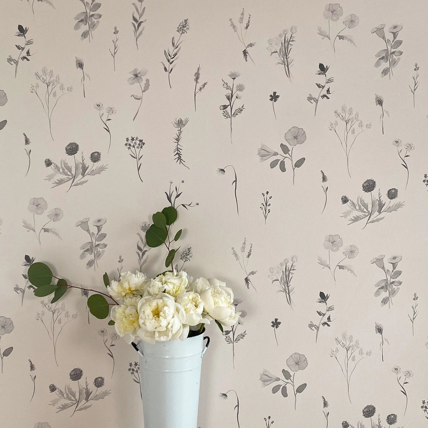 A vase of flowers stands in front of a wall covered in a painterly flower print in shades of gray on a cream field.