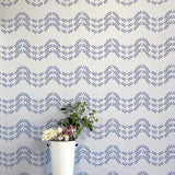 A vase of flowers stands in front of a wall covered in a curving floral stripe print in shades of blue on a cream field.