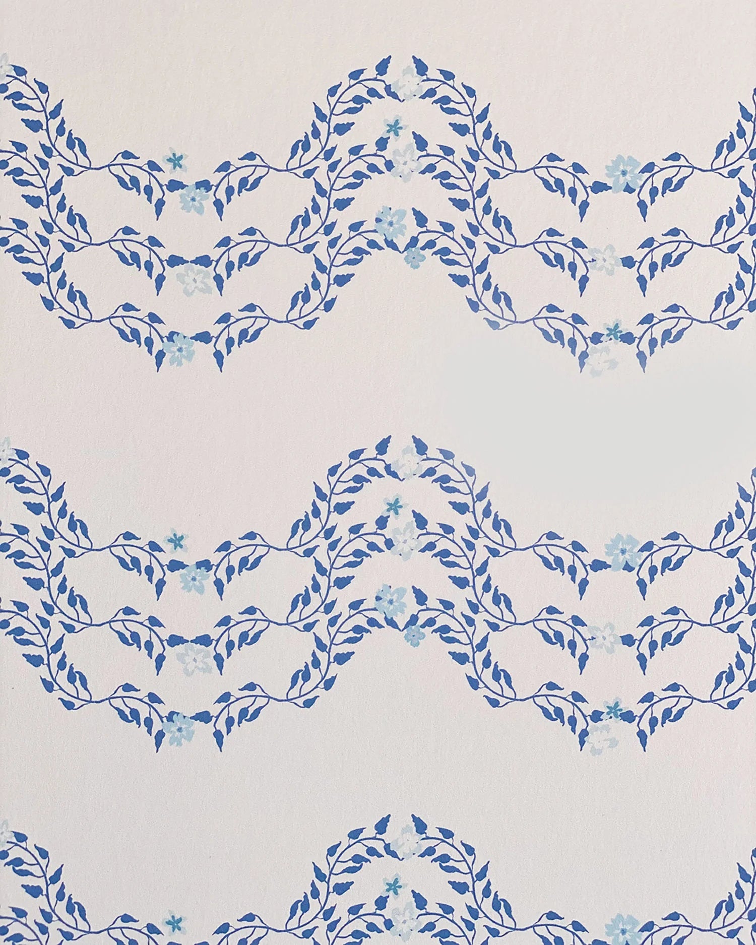 Detail of wallpaper in a curving floral stripe print in shades of blue on a cream field.