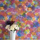 A vase of flowers stands in front of a wall covered in a dense photorealistic floral print in multicolor neon shades.