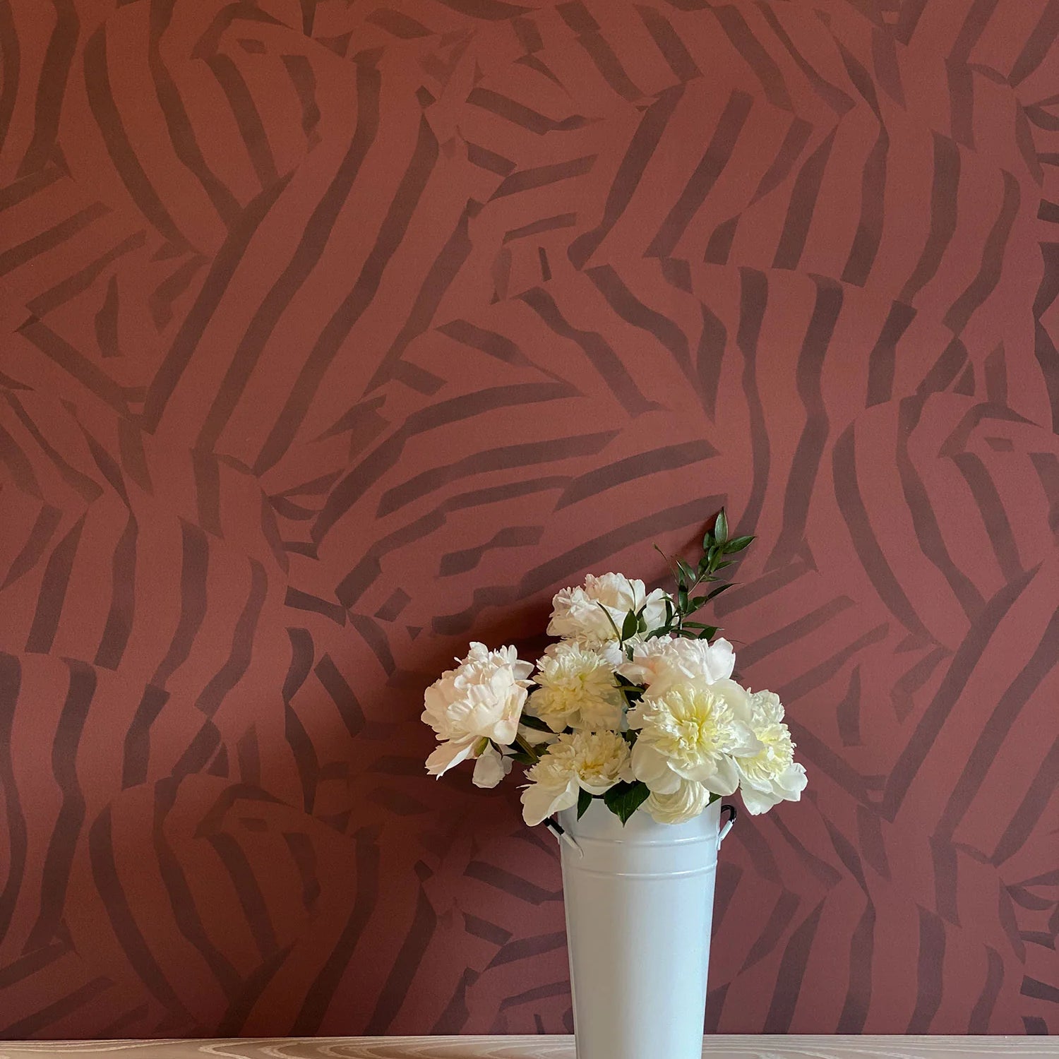 A vase of flowers stands in front of a wall papered in a playful broken stripe print in purple on a red field.