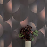 A vase of flowers stands in front of a wall covered in an abstract curvilinear print in mottled black, pink and cream.