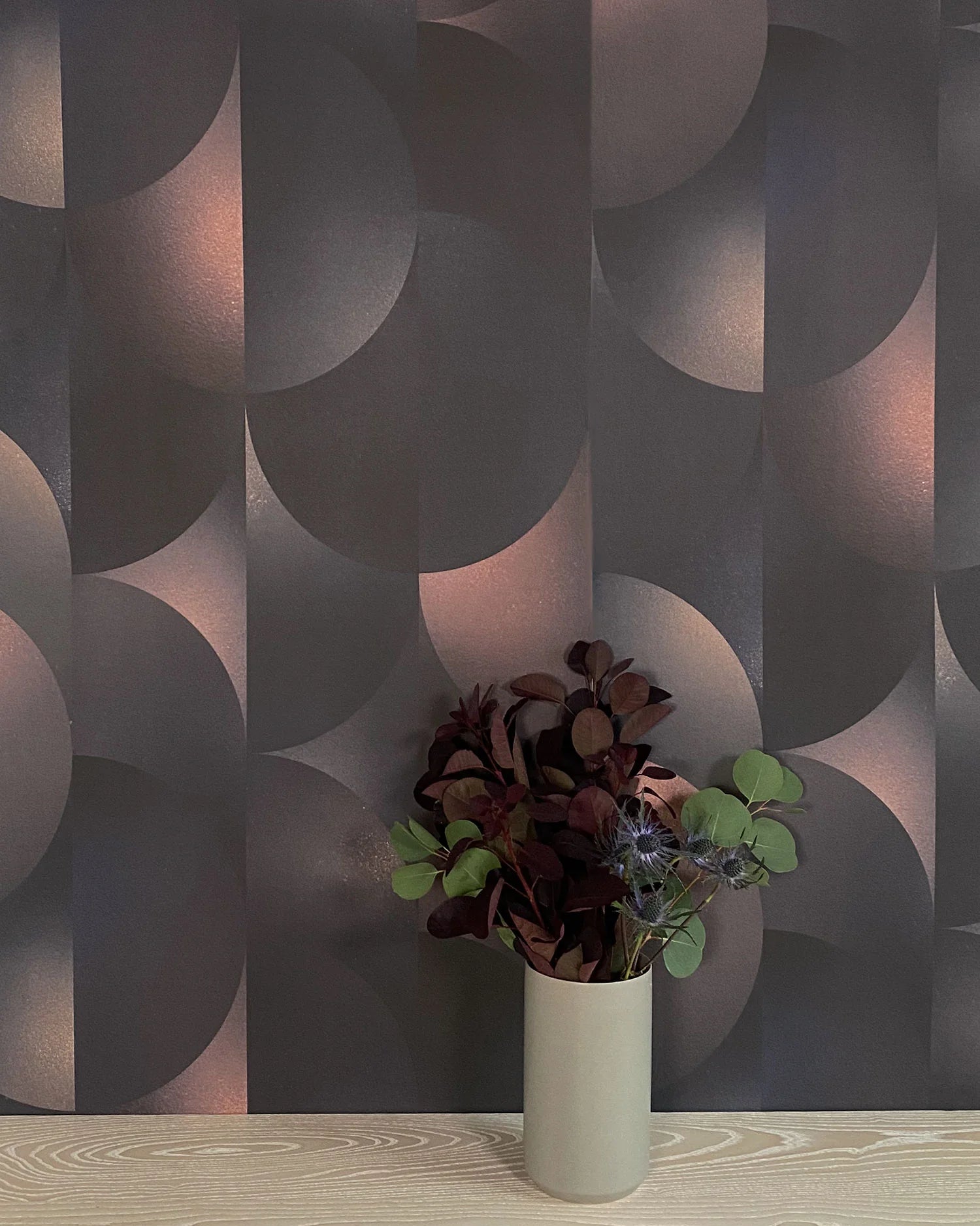 A vase of flowers stands in front of a wall covered in an abstract curvilinear print in mottled black, pink and cream.